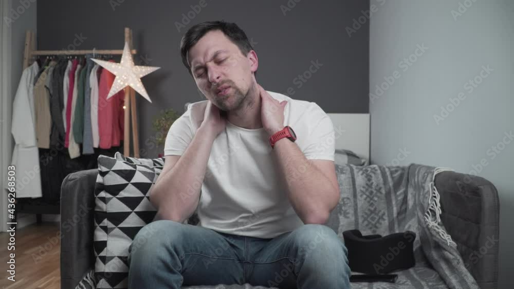 Guy wearing neck brace to support neck at home on couch. Caucasian man