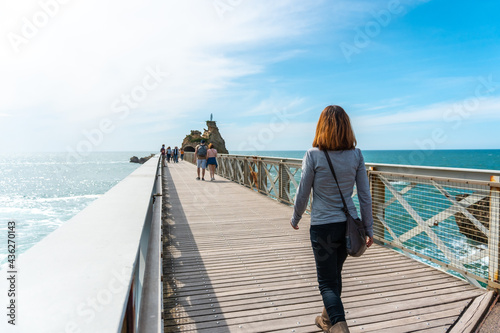 A young woman strolling along the wooden bridge together at Plage du Port Vieux in Biarritz, on vacation in southeastern France. Biarritz, department of Pyrenees-Atlantiques