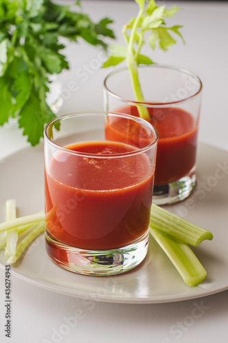 Two glasses with tomato juice, parsley and selera on a white background photo