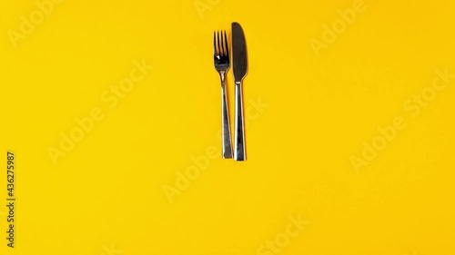 Time to eat, fork knife, alarm clock on yellow background. Stop motion animation, top view