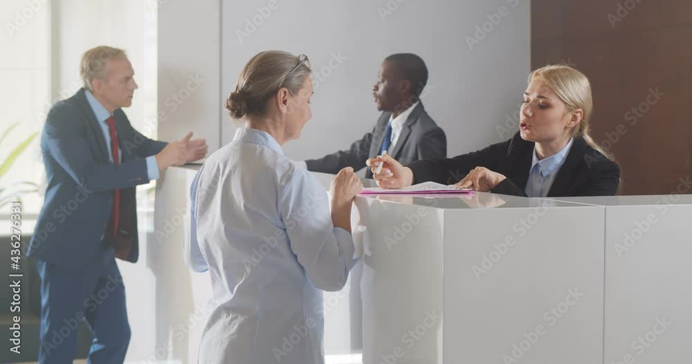 Mature businesswoman signing document at reception desk in business center