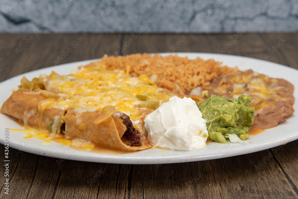 Taquitos rancheros smothered in melted cheese cooked to perfection and served with rice and beans on a plate