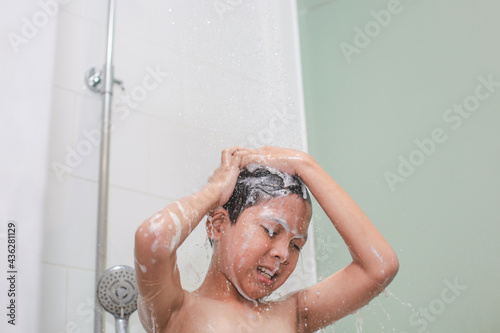 A boy rubbing hair using shampoo with foam on his face during shower in the bathroom