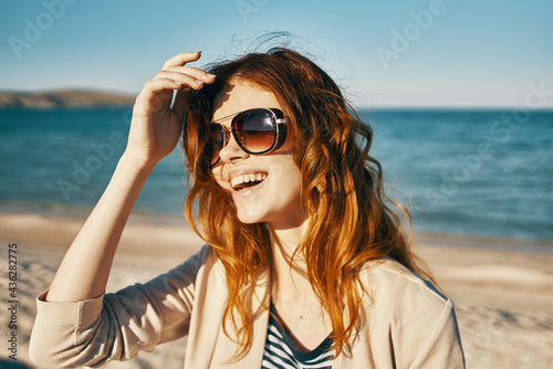woman with red hair and sunglasses laughs in nature on the beach near the sea