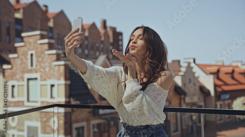 happy young woman taking selfie and sending air kiss.