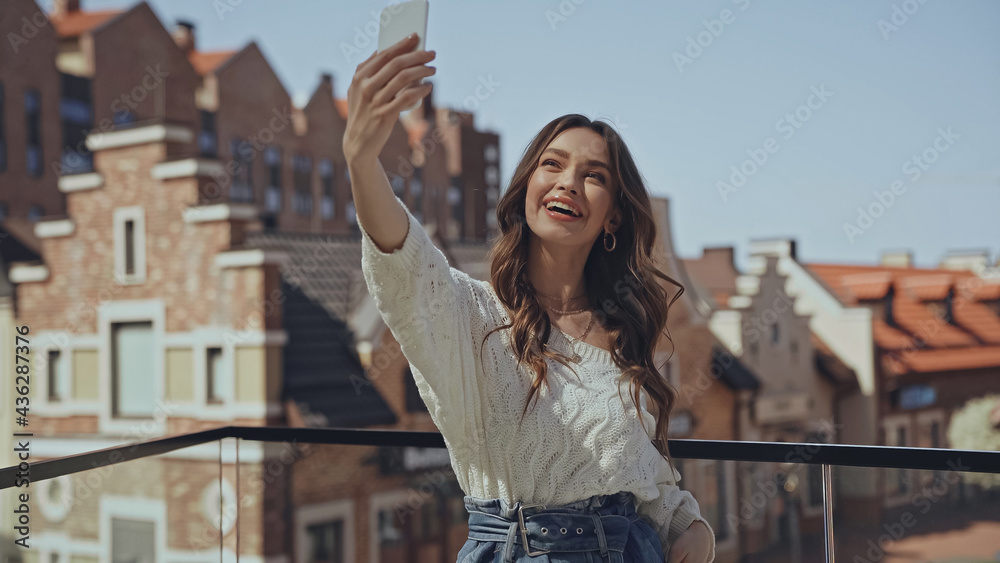 amazed young woman taking selfie near blurred buildings.