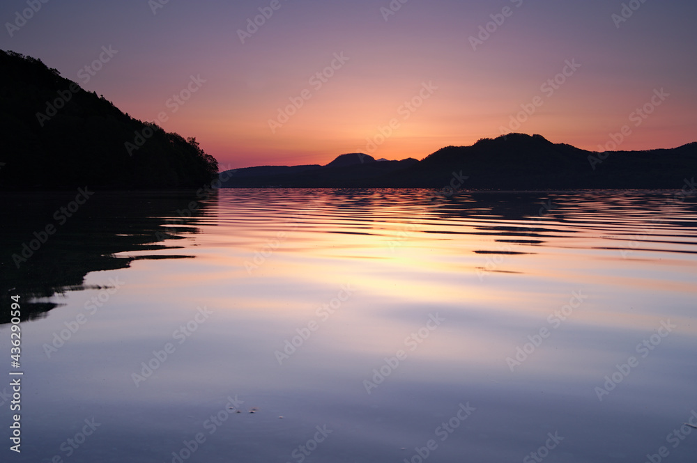 Obraz premium 薄いオレンジ色の夜明けに穏やかな湖面の湖。