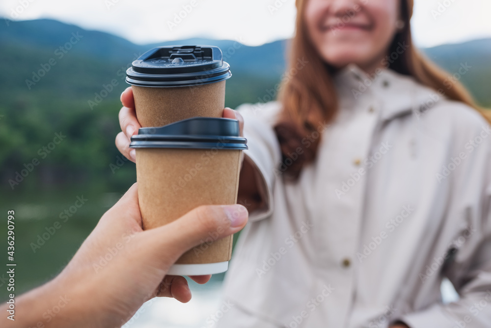 Closeup image of a couple holding and clinking coffee cup together while traveling mountains and the lake