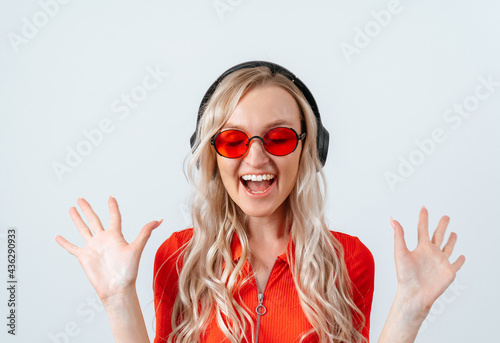 Portrait of a happy young woman with closed eyes, standing with open palms, happy blonde in red glasses. © cinematri