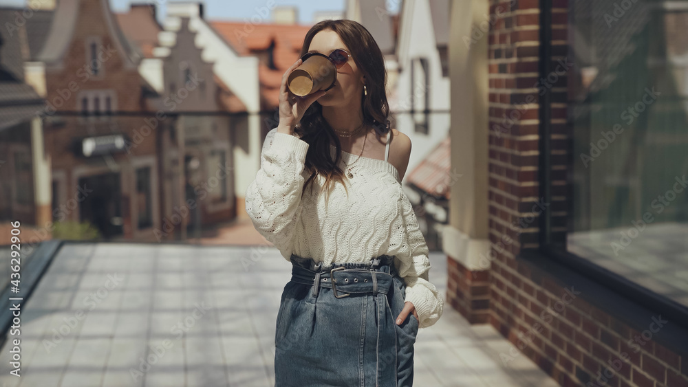 stylish young woman in sunglasses drinking coffee to go outside.