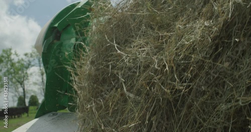 Slow motion close up of hay being unrolled from a tractor pulling a Hustler Chainless while a herd of angus cattle graze in the background photo