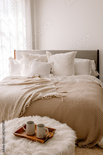 Warm and inviting loft space with a bed covered in soft fluffy pillows and blankets. Two cups of coffee on a tray in the foreground. 