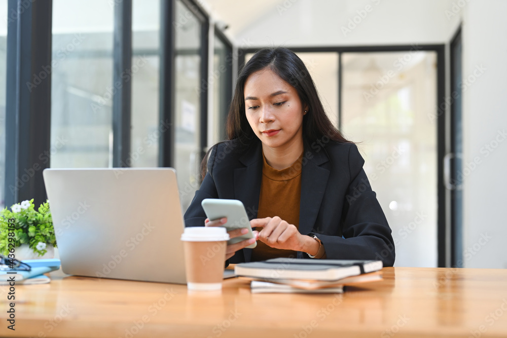 Confident businesswoman using mobile phone while taking a break in office. Confident businesswoman using mobile phone while taking a break in office.