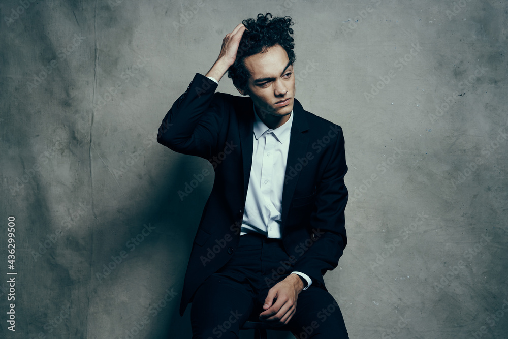 curly haired guy in a suit sitting on a chair fashion modern style jacket