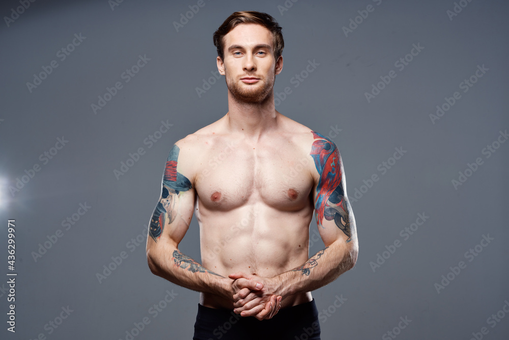 handsome man with a naked pumped-up torso tattoos on his arms holds his hands on his belt