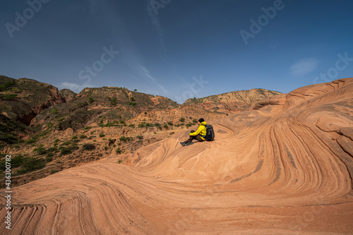 A traveler sits on the wave landform rocks. 