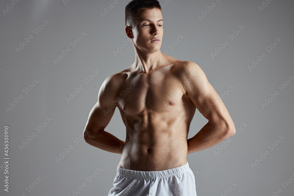 athlete with pumped up abs holding hands behind his back on gray background athlete with pumped up abs holding hands behind his back on gray background