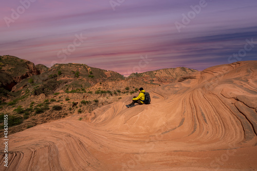 A traveler sits on the wave landform rocks. 
