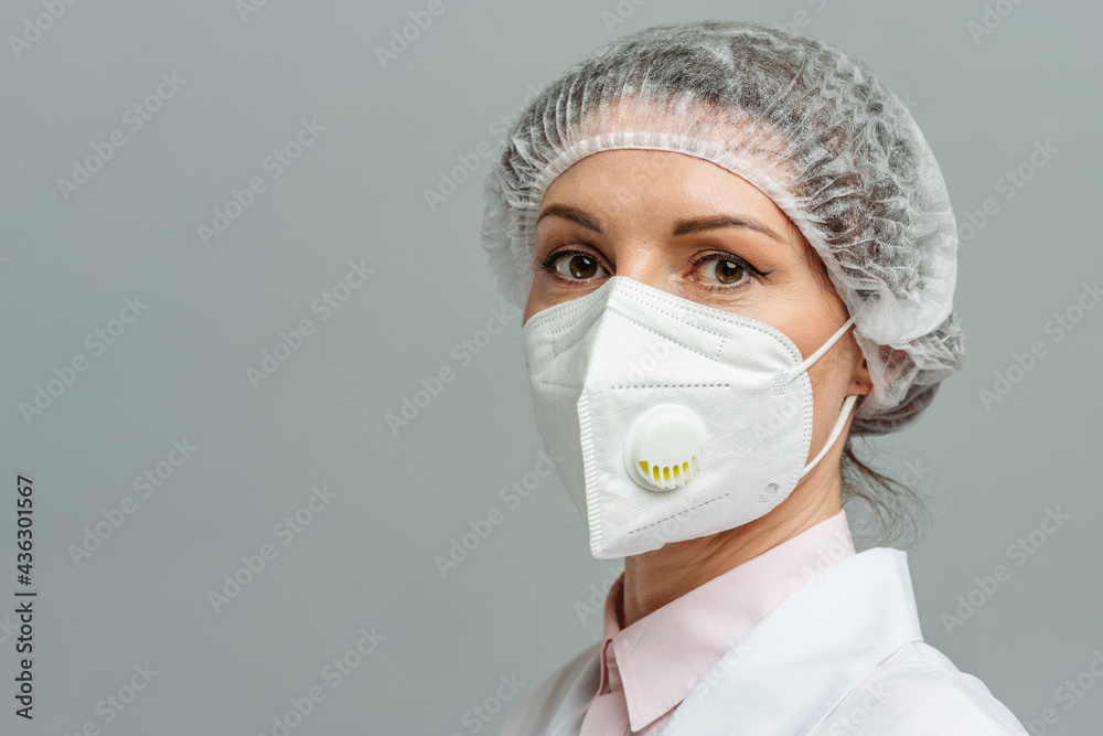 Portrait of an unhappy young woman doctor in a medical mask on a gray background. The doctor's tired eyes. The concept of coronavirus. Portrait of an unhappy young woman doctor in a medical mask on a gray background. The doctor's tired eyes. The concept of coronavirus.