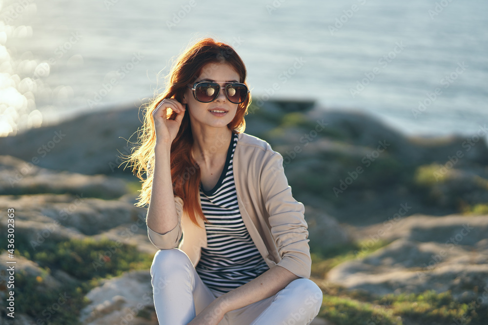 woman in a jacket and t-shirt in the mountains near the sea on the beach and glasses on her face