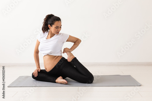 Young flexible pregnant woman doing gymnastics or yoga on rug on the floor on white background. The concept of preparing the body for easy childbirth