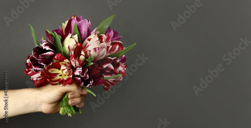 Hand with a bouquet of beautiful flowers on a gray background. Horizontal banner