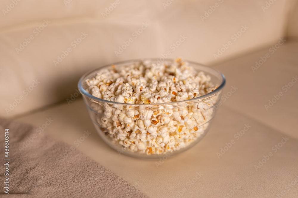 Bowl of popcorn for watching a film on a beige couch. Snacks and unhealthy junk food concept Bowl of popcorn for watching a film on a beige couch. Snacks and unhealthy junk food concept