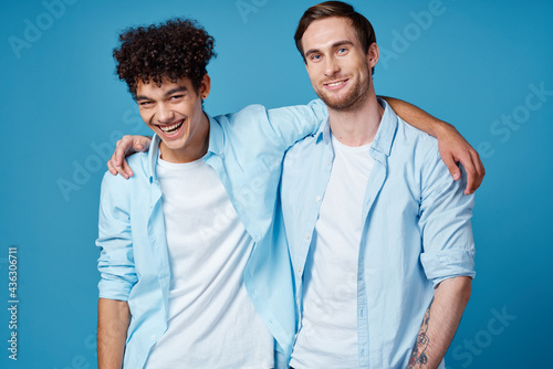 guy with curly hair in a shirt and a t-shirt on a blue background and a young man friends fun