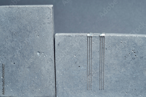 Studio shot of stylish minimalist sterling silver jewelry dangle chain earrings on concrete element isolated over gray background