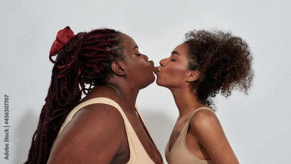 Portrait of plus size and slim african american women in underwear making kiss gesture to each other, posing together isolated over gray background