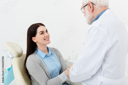 smiling patient in dental chair holding hands of senior doctor in clinic.