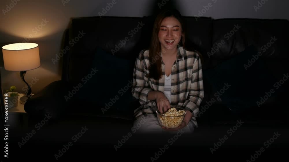 Funny young woman watching TV and eating popcorn on sofa at night Funny young woman watching TV and eating popcorn on sofa at night