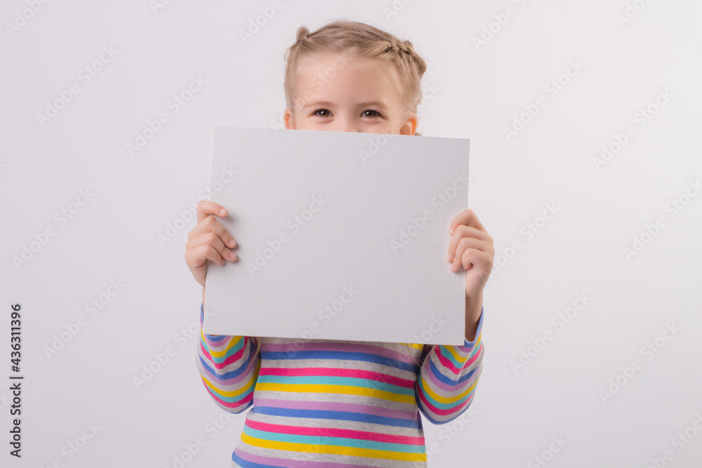 a happy cute little blonde girl with pigtails in a colored jacket holds a white sheet in her hands and smiles a happy cute little blonde girl with pigtails in a colored jacket holds a white sheet in her hands and smiles