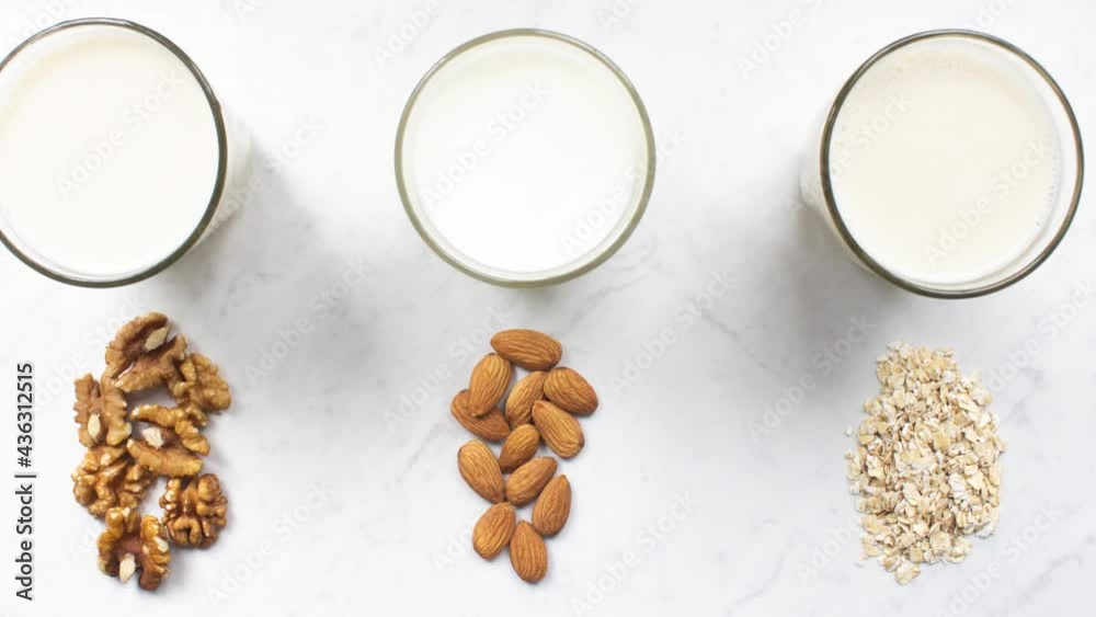Motion picture of glass of almond, walnut, oat milk on marble background top view. Nut vegan milk. Lactose-free, dairy free milk. Hypoallergenic drink. Healthy diet and nutrition