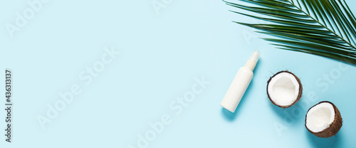 halves of coconut, palm leaf and spray bottle on a blue background. Top view, flat lay. Banner