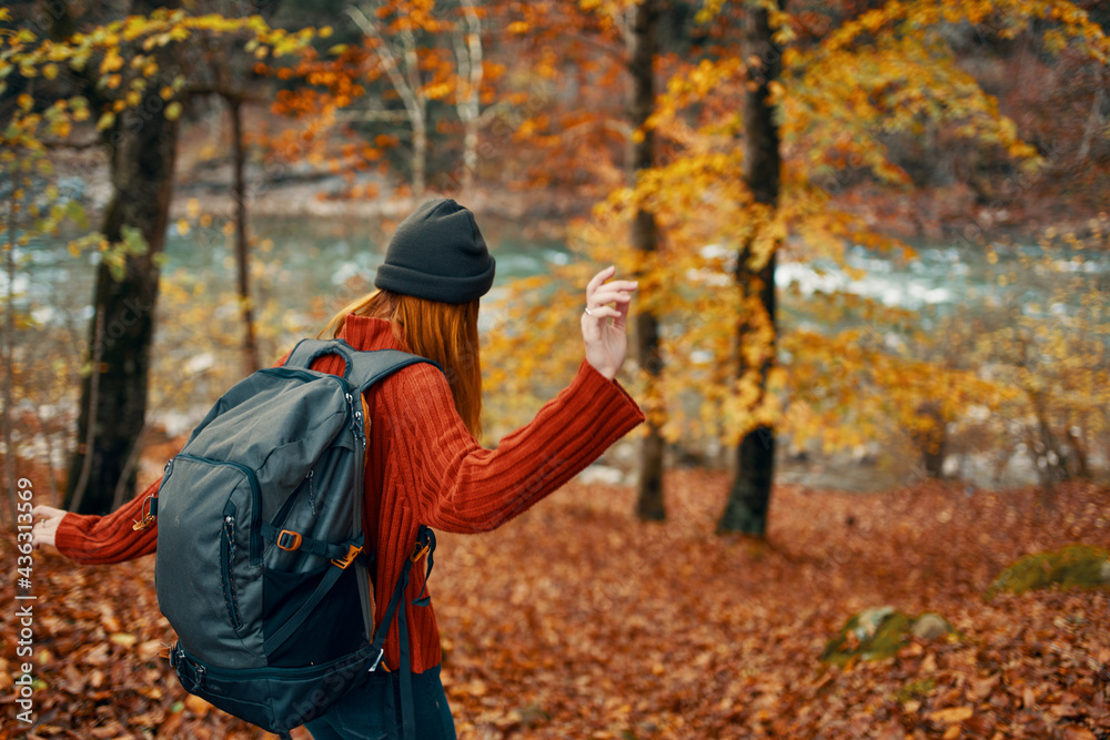 woman hiker with backpack in autumn forest near mountain river and fallen leaves