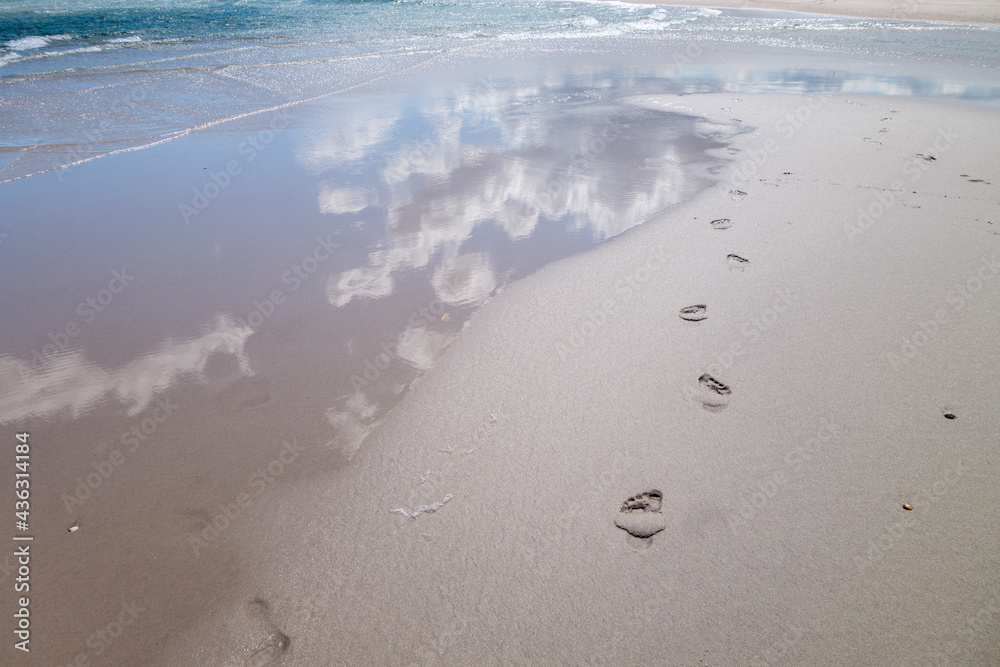 beach wet sand with fresh human bare footprints and blue cloud sky reflection and water waves beach wet sand with fresh human bare footprints and blue cloud sky reflection and water waves