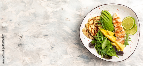 Buddha bowl with pineapple salad, grilled chicken breast, halloumi, avocado, green rocket salad and lime. Long banner format, top view