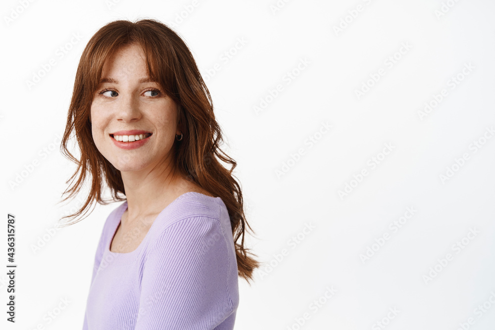 Portrait of stylish natural young woman with freckles, white smile, turn head and look behind shoulder at logo banner, staring at advertisement with happy face, white background Portrait of stylish natural young woman with freckles, white smile, turn head and look behind shoulder at logo banner, staring at advertisement with happy face, white background
