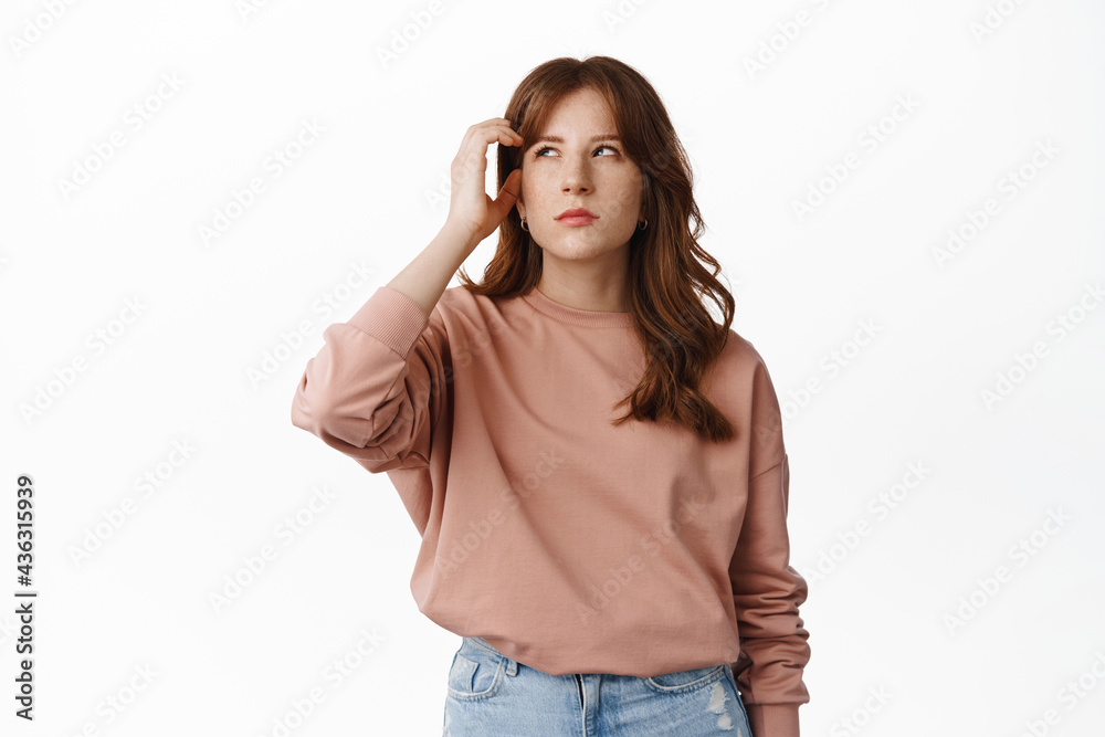 Image of thoughtful ginger girl, scratch head and look aside thinking, pondering about something, standing in casual outfit against white background Image of thoughtful ginger girl, scratch head and look aside thinking, pondering about something, standing in casual outfit against white background