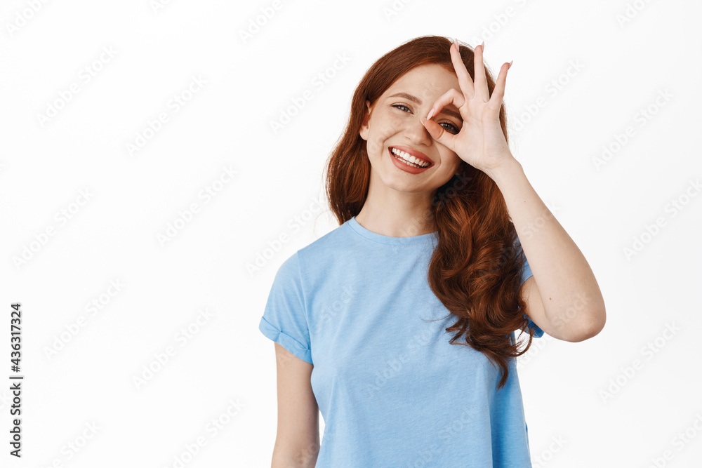 Happy candid girl with white smile, showing okay gesture near eye, praise good quality of services, recommend something good, approve and like, standing over white background Happy candid girl with white smile, showing okay gesture near eye, praise good quality of services, recommend something good, approve and like, standing over white background