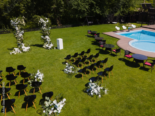 Wedding arch with flowers and greenery, decor and chairs in villa swimming pool. Drone photography.