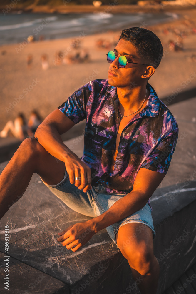Summer lifestyle, of a young Latino man enjoying summer vacation. with purple flower shirt and sunglasses, by the beach Stock-foto | Adobe Stock