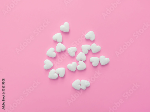White pills in the shape of hearts on a pastel pink background