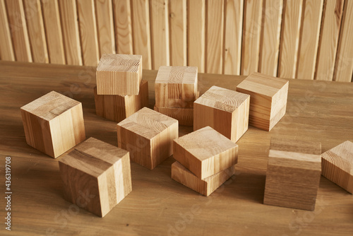 wooden cubes of different sizes lie on the table against the background of a wooden wall © Hanna