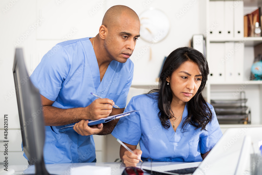 Obraz premium Two focused doctors working with patient records on laptop in modern medical office