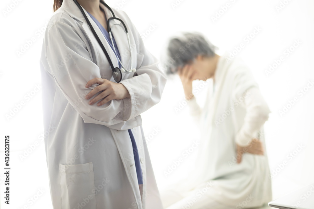 Confident doctor standing with arms folded,patient in background Confident doctor standing with arms folded,patient in background