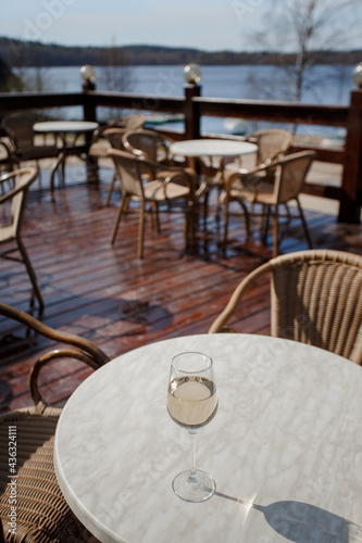 A glass of white wine on a white table on the terrace. Glare from a glass of wine and sunbeams