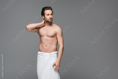 shirtless man wrapped in towel standing isolated on grey.