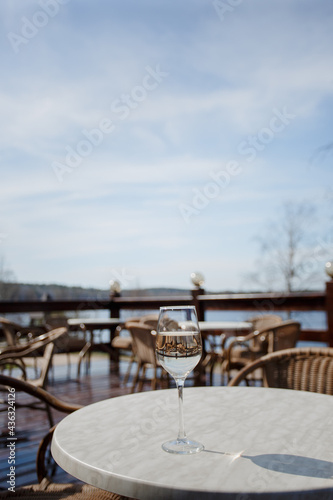 A glass of white wine on a white table on the terrace. Glare from a glass of wine and sunbeams